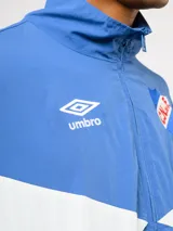 Buzo deportivo de nylon con medio cierre frontal y cuello alto. Presenta un diseño de bloques de color en azul, blanco y bordó, con el escudo del Club Nacional de Football y el logo de Umbro en el pecho.