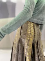 Falda larga plisada color marrón con estampado geométrico dorado en la parte superior y bolsillos laterales.