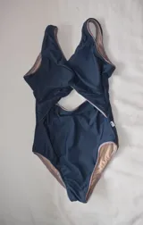 Malla enteriza con diseño cut-out en la cintura y detalle de nudo en el frente. Presenta una combinación de colores azul oscuro con bordes en tono lila y forro interno en color nude.