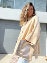 Saco tejido de punto en color crudo, con diseño holgado, mangas tres cuartos y bolsillos frontales grandes confeccionados en cuero metalizado plateado.