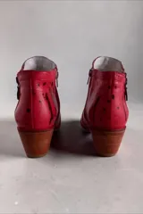 Bota corta de cuero rojo con diseño pintado a mano, inserciones laterales de cuero nonato dorado y negro, taco cuadrado de madera y doble cierre lateral con tiradores metálicos personalizados.