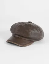 Boina estilo cap con visera, confeccionada en cuero vegano de color marrón oscuro. Presenta un diseño estructurado con costuras visibles en la parte superior.