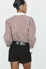 Camisa de manga larga con estampado de rayas verticales en tonos marrón y beige. Presenta cuello solapa y puños anchos en color blanco a contraste, con cierre frontal de botones.