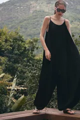 Mono de mujer color marrón oscuro, con escote redondo y tirantes finos. El tejido es satinado y plisado verticalmente. El pantalón es estilo bombacho con bajo abullonado ajustado con botón.