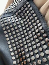 Bolso tote negro de cuero sintético con diseño holgado y dos asas de hombro. Presenta tachas metálicas redondas plateadas cubriendo la parte superior del cuerpo del bolso.