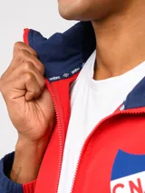Campera deportiva Umbro del Club Nacional de Football, modelo Summit. Presenta un diseño con bloques de color en azul, rojo y blanco, con capucha, cierre frontal y bolsillos laterales con cierre. Incluye el logo de la marca y el escudo del club en el pecho.