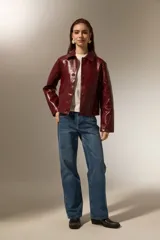 Chaqueta de eco-cuero negro con acabado brillante, cuello camisero, cierre frontal con botones y mangas largas.