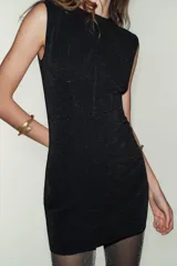 Vestido corto negro con brillo, cuello redondo y manga sisa. Presenta un detalle de aplicación de hilo metalizado y bajo recto.