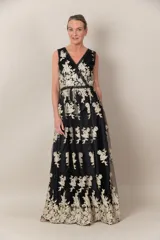 Vestido largo de tul negro con bordado dorado de flores. Tiene escote en V cruzado, sin mangas y falda amplia.