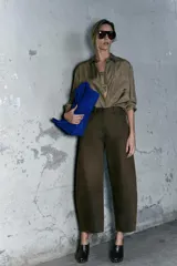 Pantalón de tiro medio color verde oliva, confeccionado en tejido con estructura de espiga. Presenta pierna ancha, trabillas en la cintura, cinco bolsillos y cierre frontal con cremallera y botón.