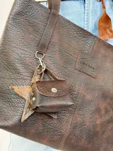 Cartera tote Chabas modelo Molly, confeccionada en cuero genuino color marrón chocolate. Presenta diseño amplio con asas largas de hombro, costuras visibles, parche frontal con logo grabado y un pequeño monedero colgante removible con broche a presión.