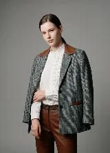 Blazer de paño de lana con diseño de pata de gallo en tonos gris y negro. Presenta cuello y detalles en los bolsillos de cuero color suela, con un corte relajado y cierre frontal de botones.