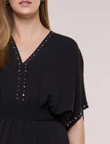 Vestido largo amarillo de corte fluido con escote en V, mangas cortas amplias y apliques de tachas en el escote y puños. Posee cintura elastizada fruncida y falda larga con tajos laterales en el ruedo.