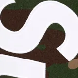 Pantalón de jogging Supreme con estampado de camuflaje woodland y logo de la marca estampado en tipografía grande y vertical en color blanco sobre la pierna izquierda.