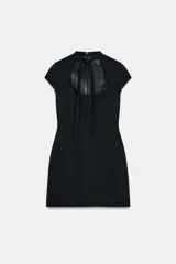 Vestido corto de color negro con escote cuadrado y detalle de lazada en el cuello. Presenta mangas cortas y cierre de cremallera oculta en la espalda.