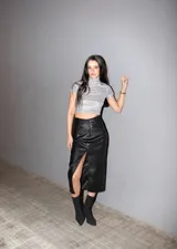 Falda midi negra de ecocuero, tiro alto, con bolsillos delanteros y traseros, abertura frontal, cierre con cremallera, botón y presillas para cinturón.