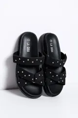 Sandalias negras de doble tira con tachas doradas, suela plana y diseño cómodo.