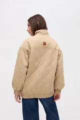 Campera bomber de gabardina con diseño capitoneado, cuello alto, cierre frontal con botones a presión ocultos y mangas abullonadas con puños elásticos.