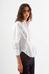 Camisa azul de algodón con finas rayas blancas verticales, cuello mao, manga larga y detalle de pinzas y botones en la zona de la cintura. Posee dos bolsillos de parche con tapa en el pecho.