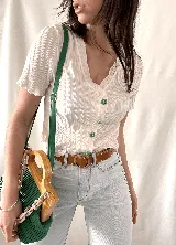 Camisa blanca con textura arrugada, escote en V, mangas cortas con volados y botones con forma de flor.