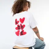 Remera blanca de corte oversize y manga corta, con estampado en la espalda que presenta corazones rojos y la palabra LOVE en letras negras.
