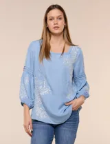 Blusa de tencel celeste con escote cuadrado, mangas tres cuartos abullonadas con puños elastizados y delicados bordados florales blancos en el frente y las mangas.
