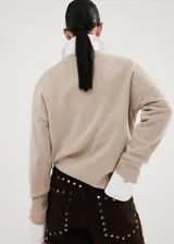 Sweater de punto color beige con cuello en V y mangas largas, diseño holgado.