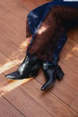 Pantalón de jean estilo wide leg, confeccionado en denim rígido de color azul oscuro. Presenta paneles laterales de encaje con diseño floral en tono rojizo y terminaciones deshilachadas en el ruedo.