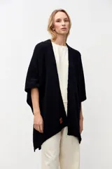 Ruana abierta de tejido de punto con textura, color negro, de corte holgado y mangas cortas. Presenta un aplique de cuero con logo en el frente y terminaciones acanaladas en el ruedo.