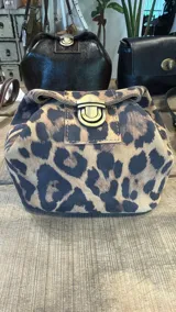Necessaire de mano con estampado animal print de leopardo, confeccionada en material tipo gamuza. Presenta un cierre frontal metálico tipo broche a presión en color bronce envejecido.