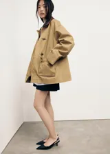 Anorak de estilo oversize en color tostado, con cuello camisero de pana en contraste. Presenta cierre frontal mediante ganchos metálicos y dos bolsillos de parche con solapa en la parte delantera.