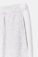 Pantalón jogger de felpa color gris claro melange, de tiro medio con cintura elástica. Presenta detalles de aplicaciones tejidas a contraste en los laterales y terminaciones con puños abullonados.