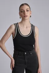 Remera negra sin mangas, tipo musculosa, con escote redondo y ribetes blancos con apliques de perlas en el contorno del cuello y las sisas.