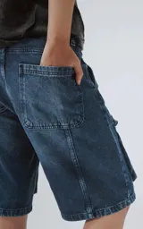 Bermuda de denim azul oscuro con lavado y efecto desgaste, corte oversize y estilo cargo con múltiples bolsillos con tapa en las piernas.