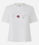 Remera de algodón color blanco, de corte clásico con cuello redondo y manga corta. Presenta un delicado bordado de tres pequeños íconos florales en el centro del pecho.