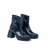 Botas cortas negras de cuero vacuno con textura tipo cocodrilo. Taco de madera forrado en cuero de 8cm, entre suela de goma de 2cm forrada en cuero, inclinación de horma de 6cm y caña de 15cm. Cierre YKK del lado interno y horma de punta cuadrada.