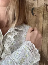Camisa de lino con estampado floral en tonos pasteles, cuello camisero, mangas largas y detalles de jabot y encaje en puños y pechera.