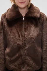 Chaqueta corta de piel sintética en color negro, con cuello clásico, cierre frontal con cremallera y mangas largas.