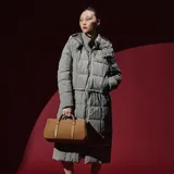 Campera larga tipo puffer color taupe, con diseño acolchado, cierre frontal, capucha y cordón ajustable en la cintura.