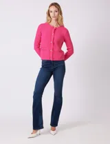Cardigan de punto color fucsia, con escote a la base, cierre frontal con botones metálicos dorados y terminaciones desflecadas. Presenta bolsillos simulados en la parte delantera y mangas largas.