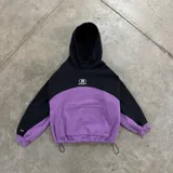 Buzo crop negro y violeta de frisa, con capucha, bolsillo frontal, estampa delantera, etiqueta bordada en el puño derecho y ajuste con tancas en la cintura.