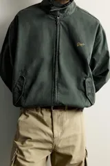 Cazadora relaxed fit de denim de algodón color verde oscuro, con cuello subido y cierre de cremallera frontal. Cuenta con bolsillos de vivo con solapa en la cadera, acabados elásticos y detalle bordado a contraste en el pecho.