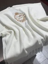 Ruana de tejido de punto con textura tipo panal en color blanco, con un escudo nacional bordado en hilo color dorado en el centro.