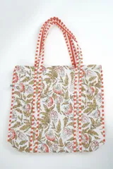 Bolso tipo tote bag acolchado, con estampado floral en tonos rosados y marrones sobre fondo blanco. Posee asas de hombro y ribetes con diseño de rayas rojas y blancas.