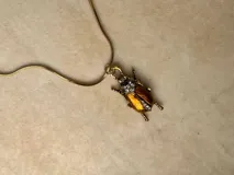 Collar de cadena fina dorada con dije en forma de escarabajo, con acabado texturizado y detalles de cristales incrustados.