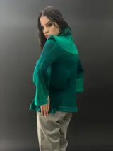 Buzo verde esmeralda de lana merino con cuello alto y mangas largas. Presenta dos texturas: afieltrada en cuello, mangas y ruedo, y tejido merino superfino en el delantero y la espalda.