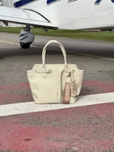 Bolso tote de cuero color crema, con doble asa de mano, cierre con botón y cinto.