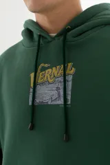 Buzo hoodie verde oscuro con estampa serigráfica frontal de alta definición con una escena urbana en estilo puntillista y logo VERNAL con efecto dorado envejecido. Corte oversize con hombros caídos, capucha doble y bolsillo canguro.