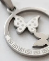 Dije circular de acero inoxidable con diseño calado de dos mariposas en el centro y detalle de guarda griega en el borde.