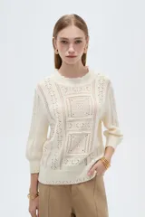 Sweater acrílico en tono natural, de corte holgado, con cuello a la base decorado con sutiles volados, mangas 3/4 y diseño tejido con motivos geométricos calados en el frente.